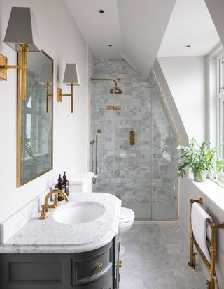 White bathroom with grey tiled shower, gold fixtures