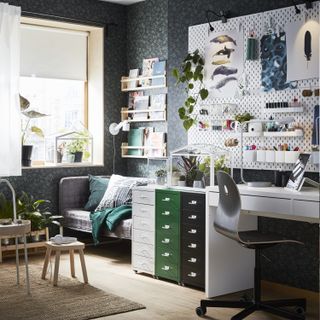 an office room/living space, with grey wallpaper, a white pegboard on the wall, multi-coloured filing cabinet, a white desk and chair, a sofa, and kids play toys on the rug