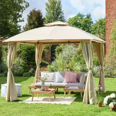 Beige gazebo on a lawn over a corner sofa with an outdoor rug and coffee table