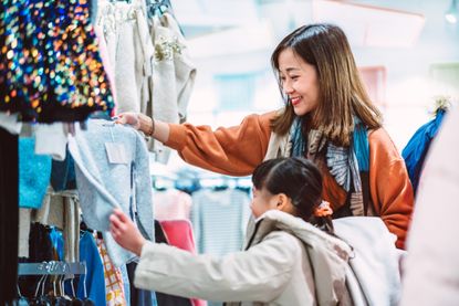 A mother shops with her daughter for clothes at a store. 