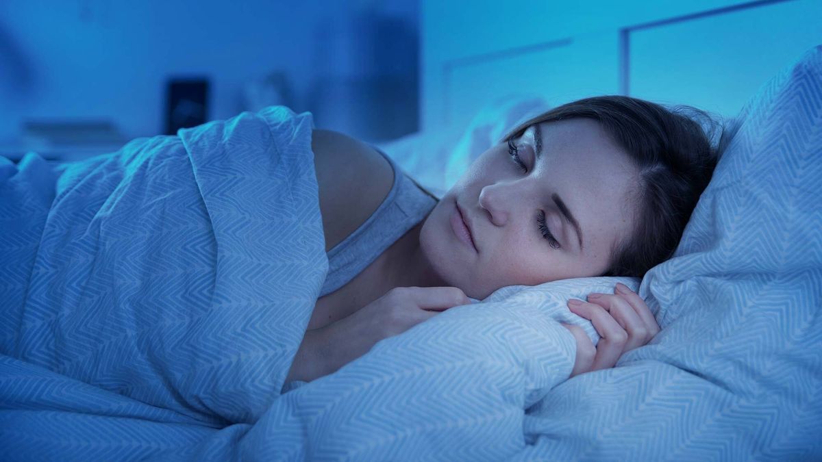 A woman with dark hair sleeps on her side in a bed dressed with cozy linens