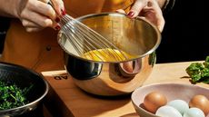 Eggs and spinach being prepped in a stainless steel mixing bowl on a wooden butcher block