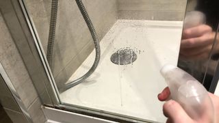 Someone spraying a vinegar water solution onto a glass panel in a shower