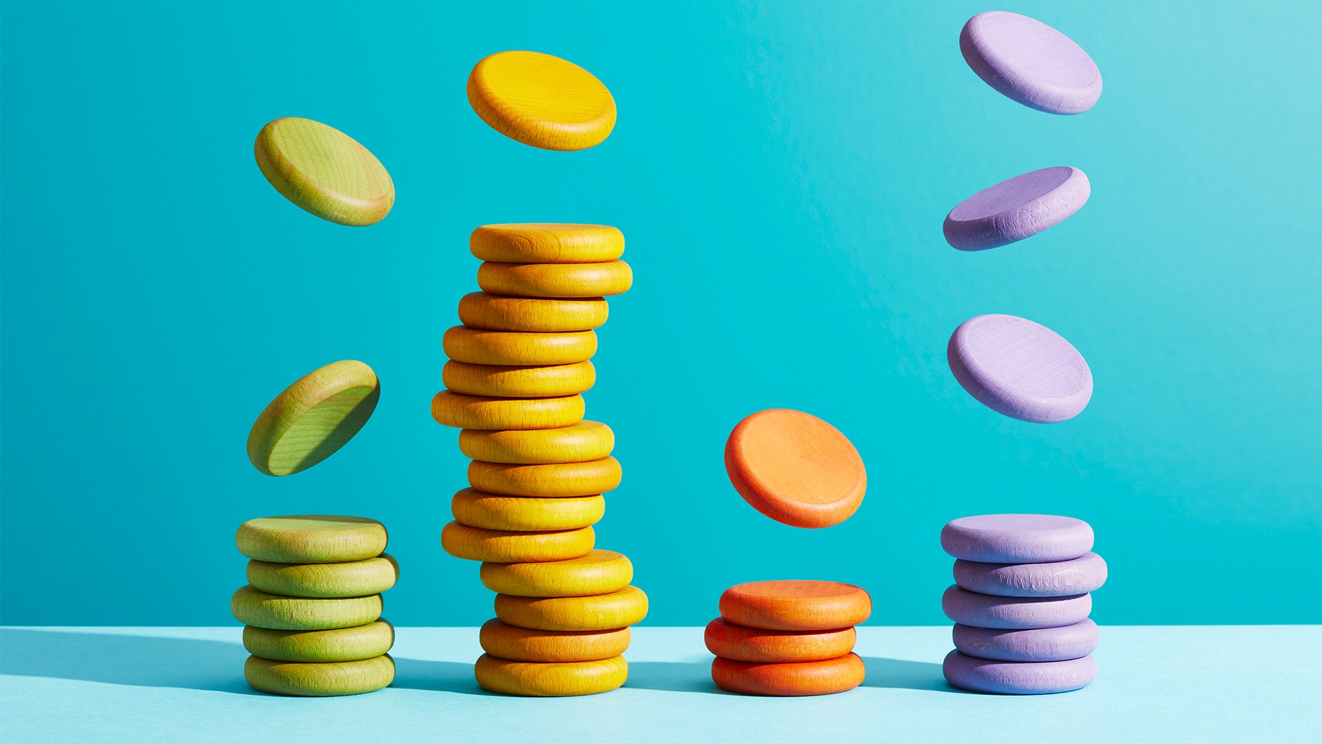 Tech spending concept image showing multi-colored coins raining down from above and stacking on top of each other. 