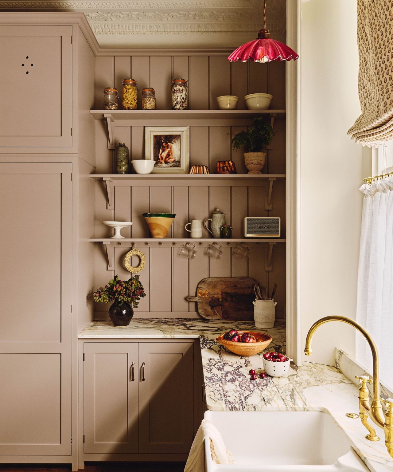 A cozy kitchen corner with mauve pink cabinetry, open shelving holding jars and ceramics, and a dramatic veined marble countertop with an integrated white sink