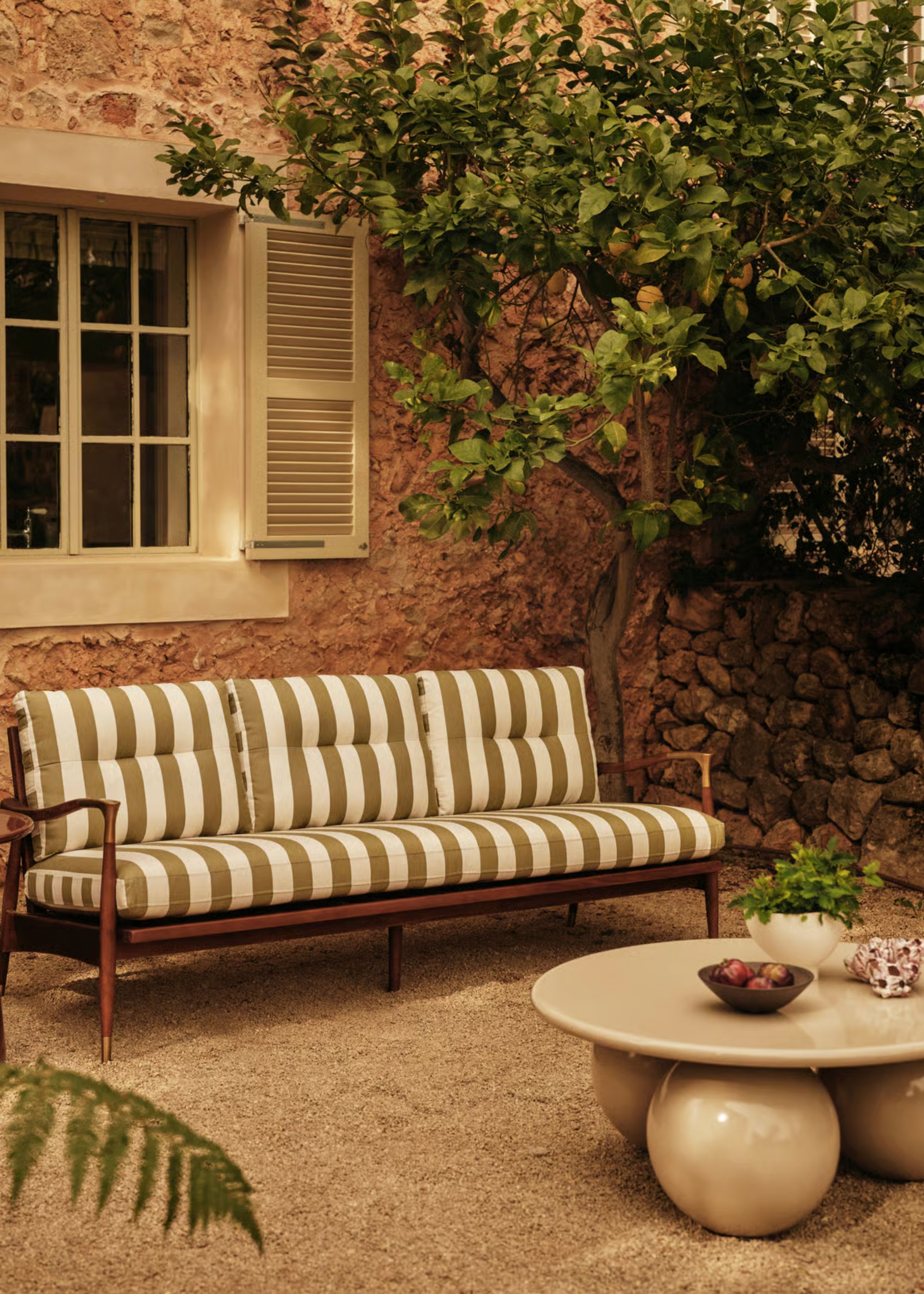 A backyard with an outdoor sofa chair and a large tree/plants next to it