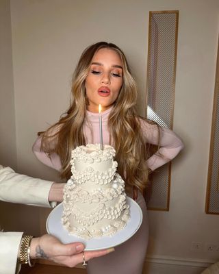 @rosiehw blowing out a candle on a birthday cake with wavy, glossy hair