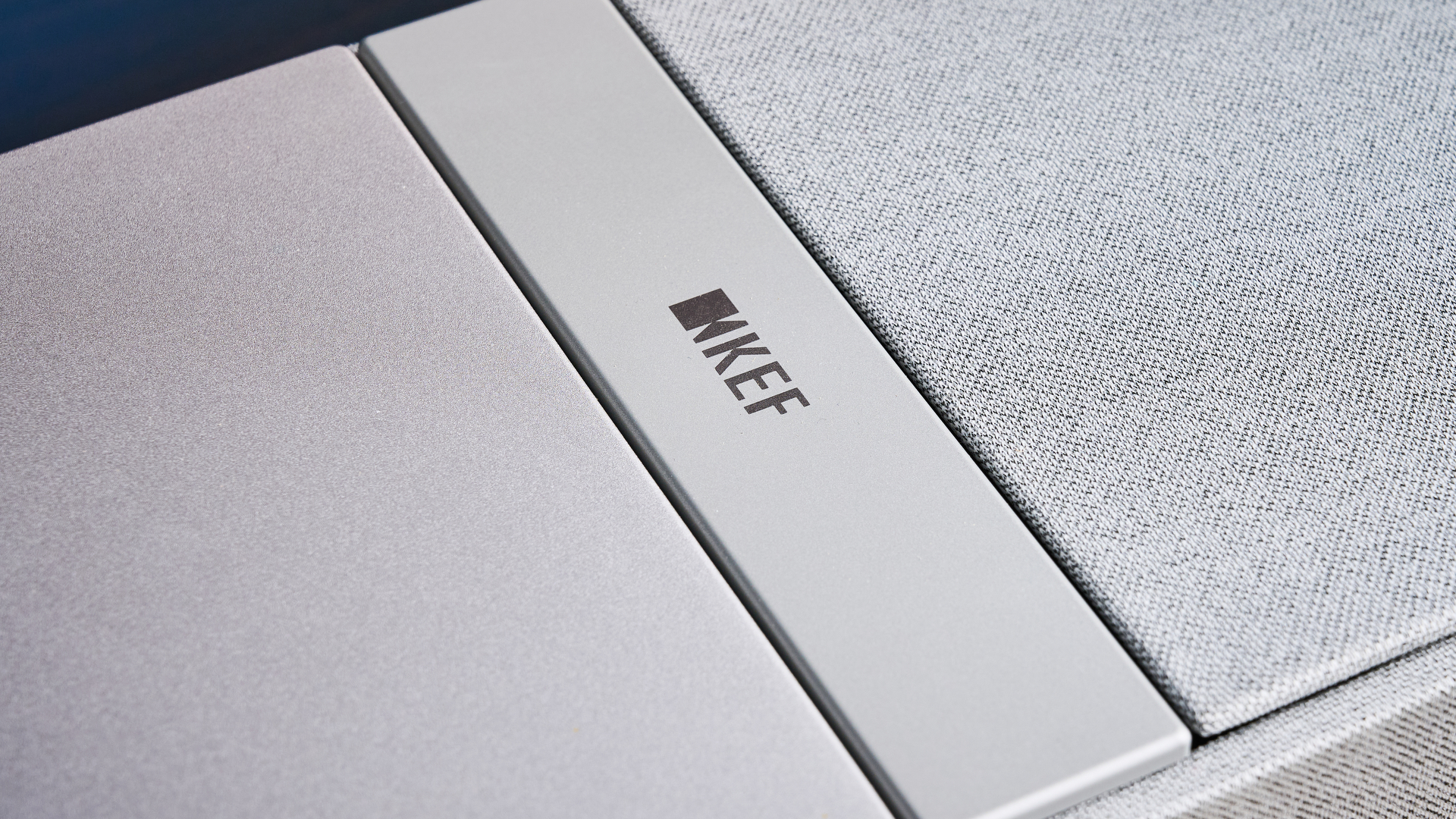the KEF XIO soundbar in gray photographed with a TV and the Tom's Guide blue background
