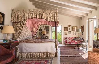bedroom with floral drapes with pink lining and painted ceiling beams with striped rug