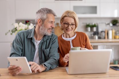A couple shares and enjoys a joyful moment with their devices in a cozy kitchen setting.