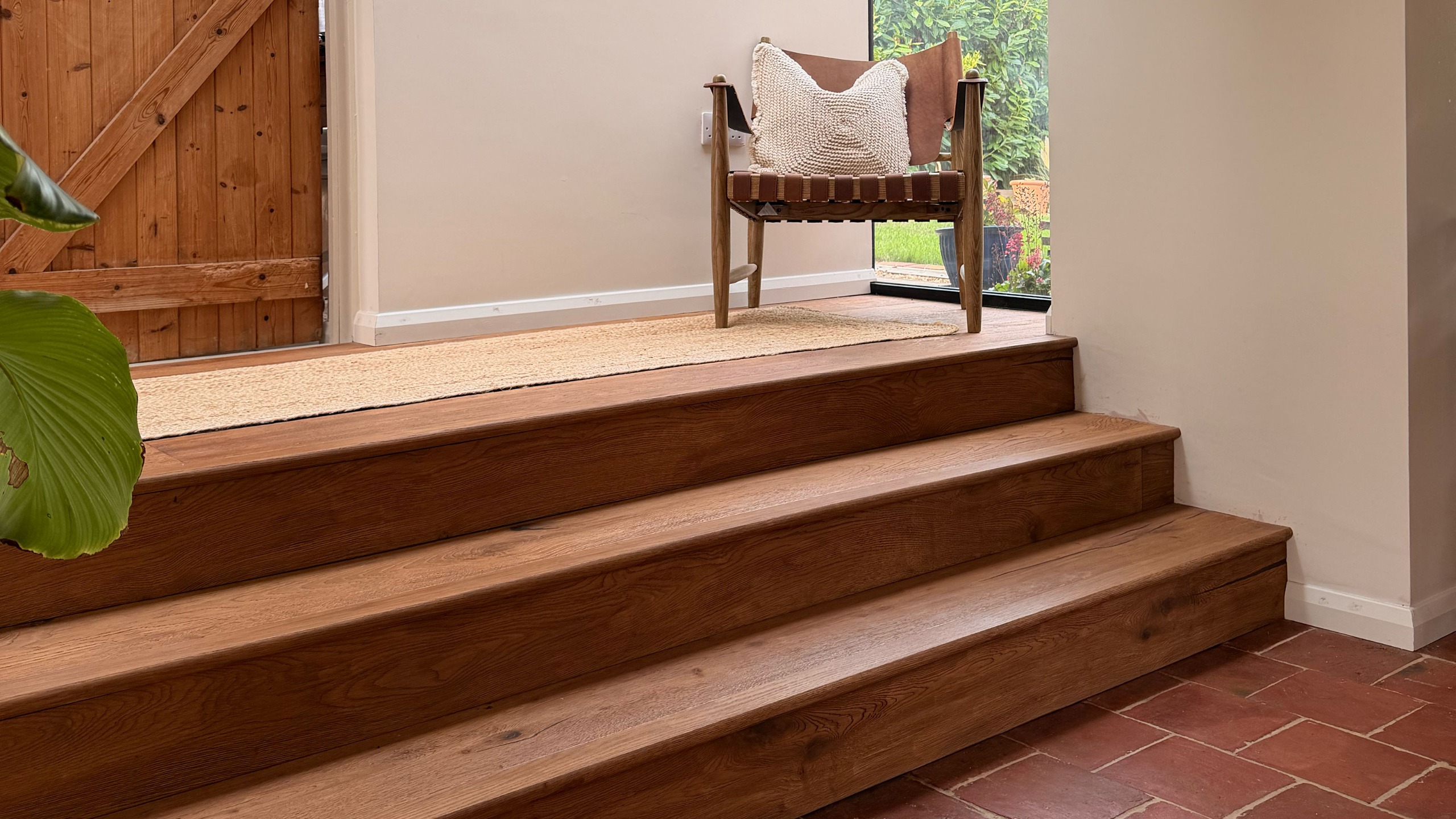 Three wooden steps leading from terracotta floored area to hallway with armchair