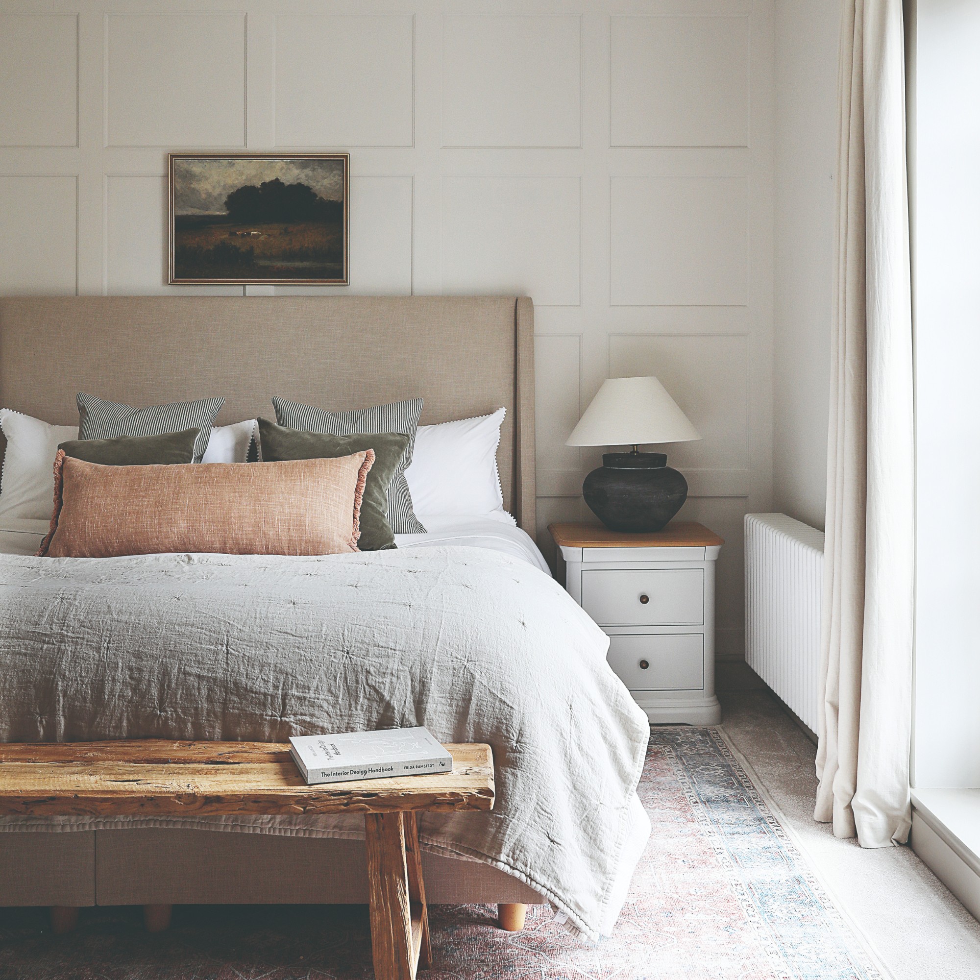 An off white-painted bedroom with a panelled feature wall behind the bed with an upholstered neutral-coloured headboard