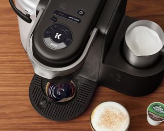 A birds eye view of a Keurig K-Café Single Serve Coffee Latte & Cappuccino Maker on a wooden table with a coffee next to it