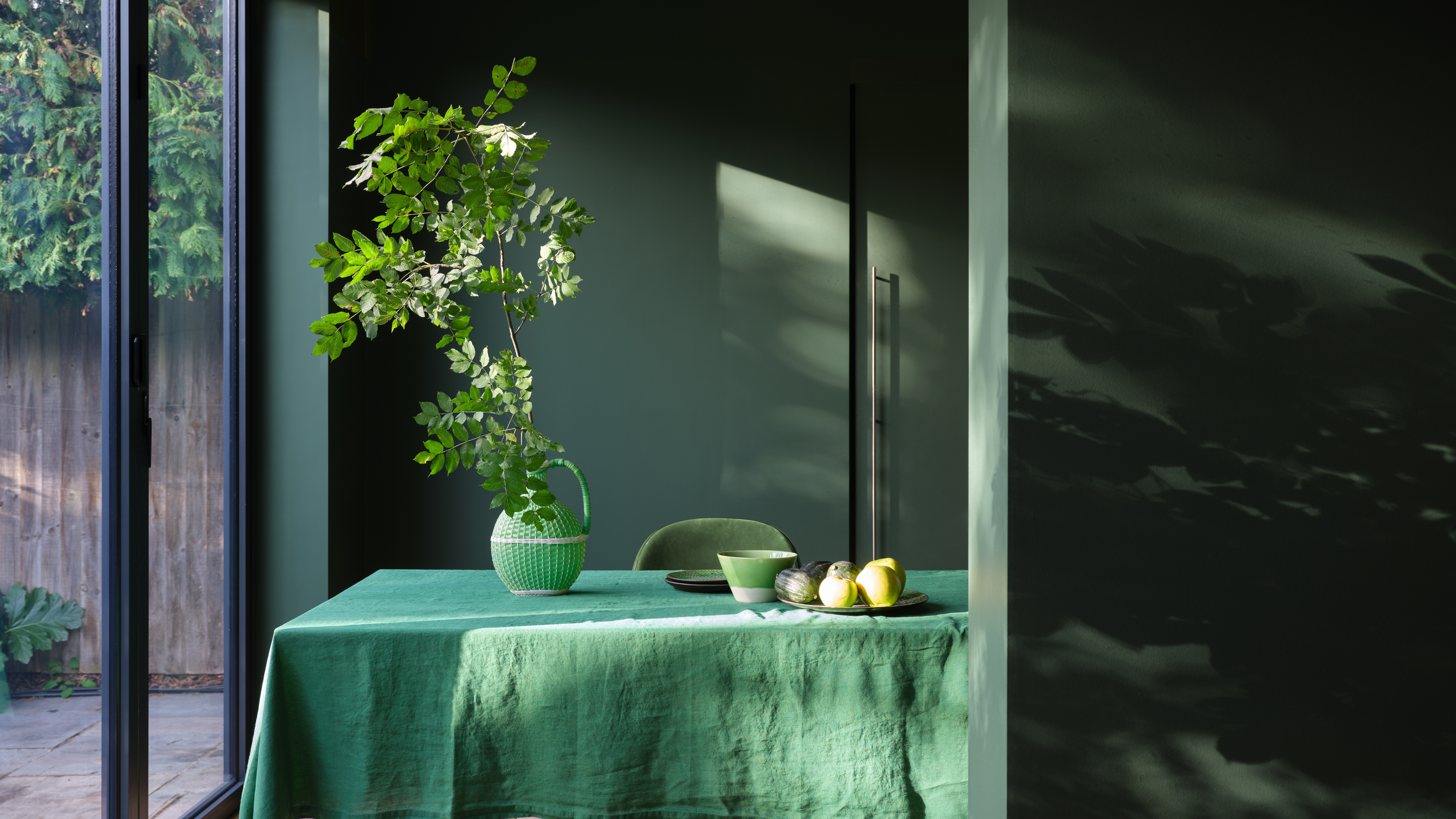 a room with green paint and a table covered in a green tablecloth with a plant on top