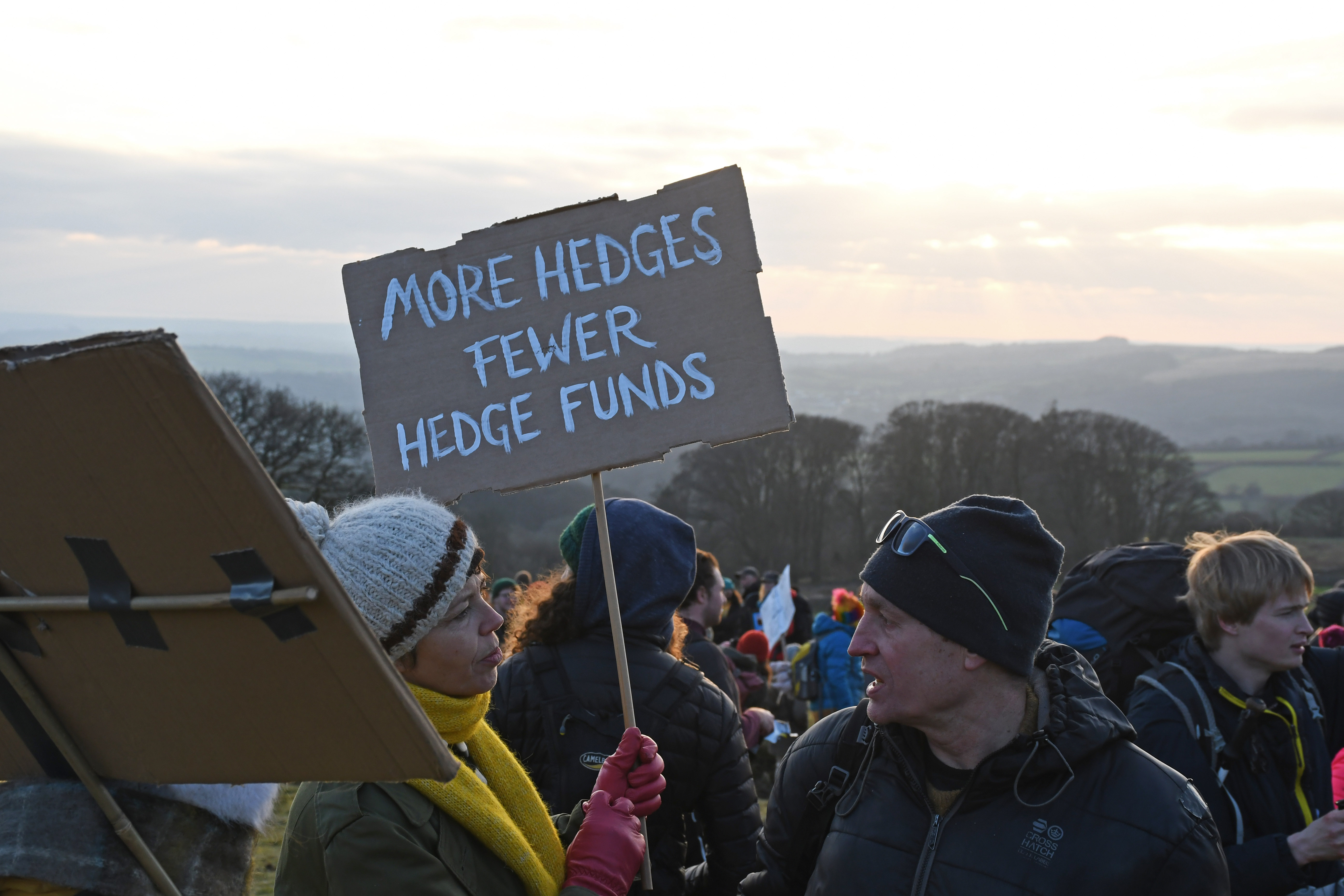Protesters hold a banner saying 'More Hedge, Fewer Hedge Funds'