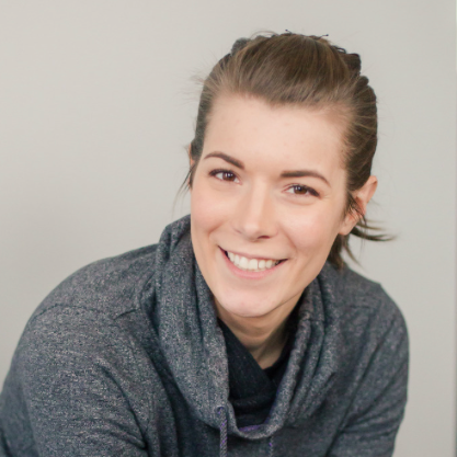 Head and shoulders of smiling woman looking at camera, her hair is tied back