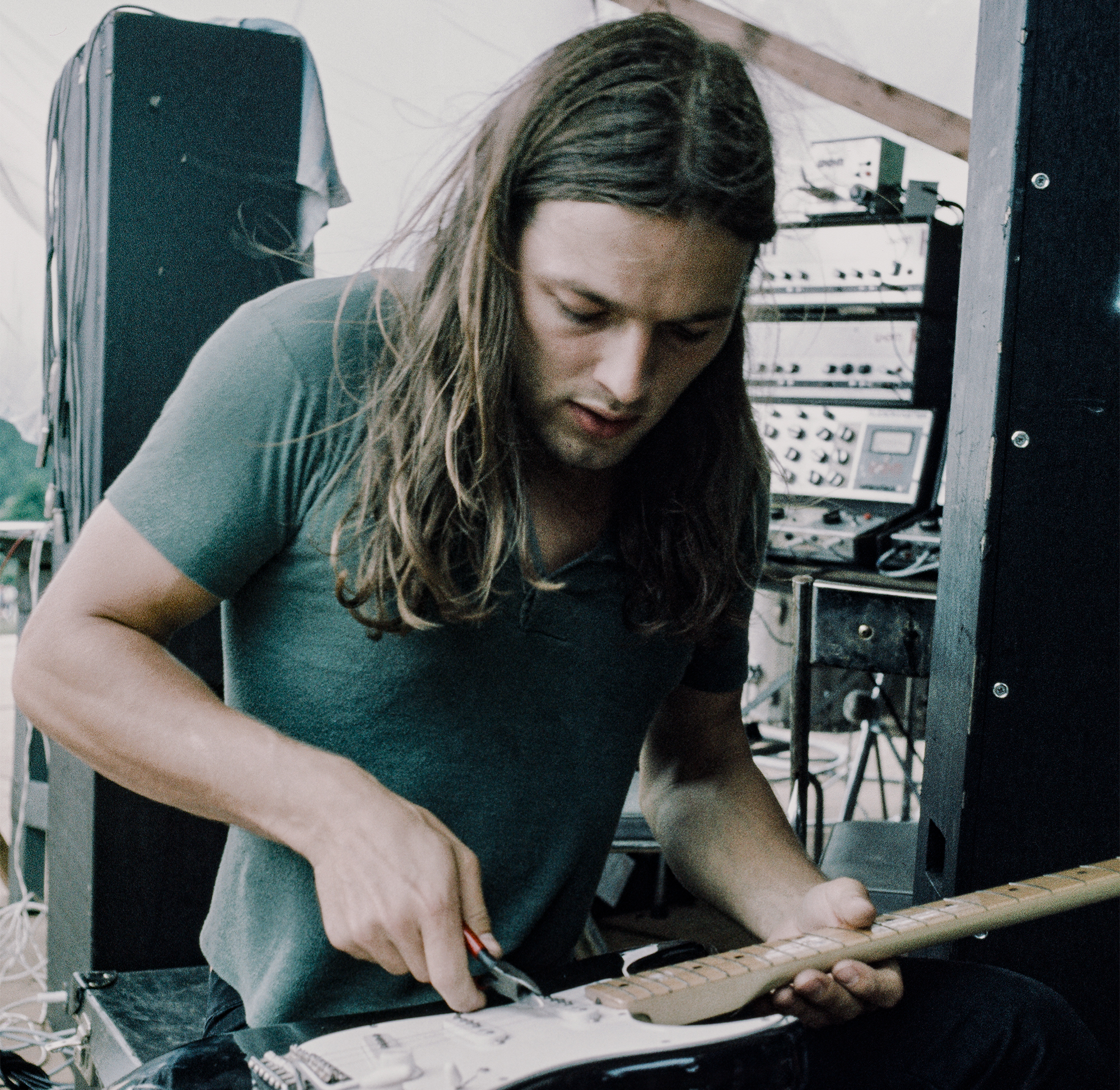 David Gilmour of Pink Floyd, working on his Fender Stratocaster guitar with pliers, backstage at Hakone Aphrodite, Japan, 6th August 1971. Behind him are the amplifiers and Audiomaster mixer for the band's WEM PA system.