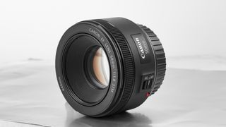 Canon EF 50mm f/1.8 STM camera lens with autofocus/manual focus switch, placed on a light reflective surface