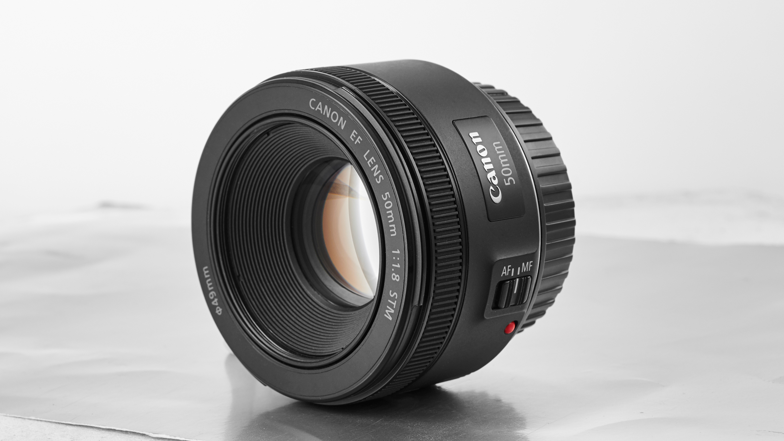 Canon EF 50mm f/1.8 STM camera lens with autofocus/manual focus switch, placed on a light reflective surface