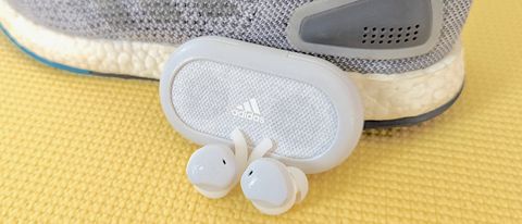 The Adidas FWD-02 wireless earbuds resting next to a pair of Adidas running shoes