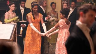 (L to R) Simone Ashley as Kate Sharma holding hands and dancing with Charithra Chandran as Edwina Sharma.