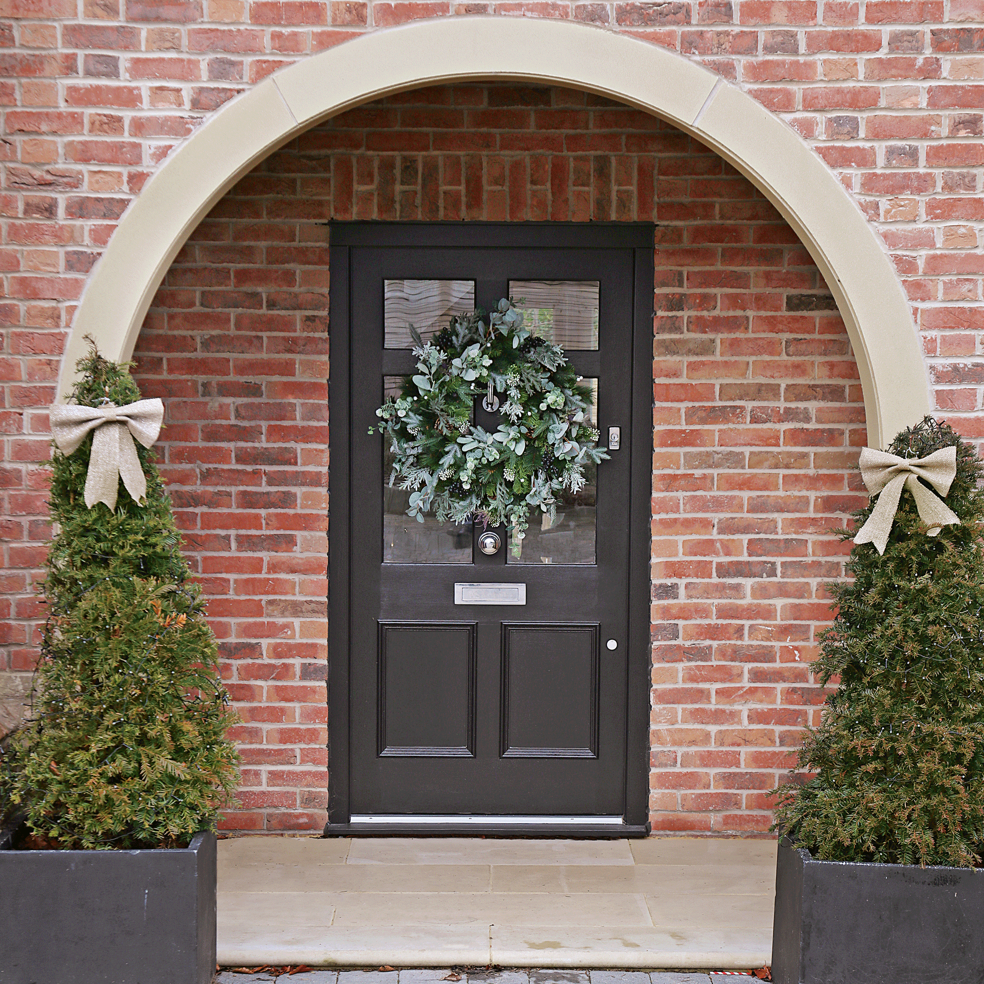 the front door of a house with a Christmas wreath on the door and two Christmas trees topped with bows