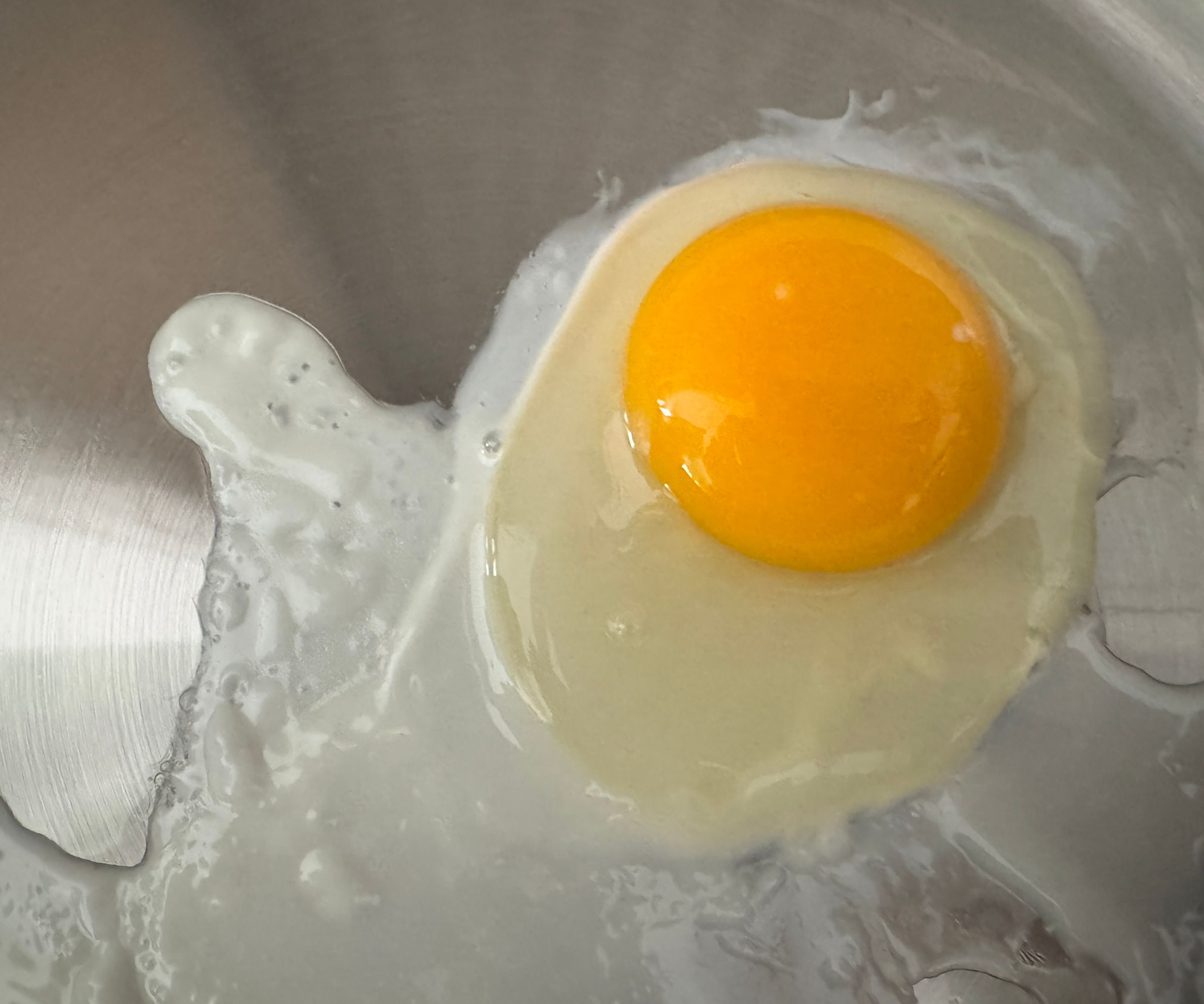 A sunny-side egg frying in a stainless steel frying pan.