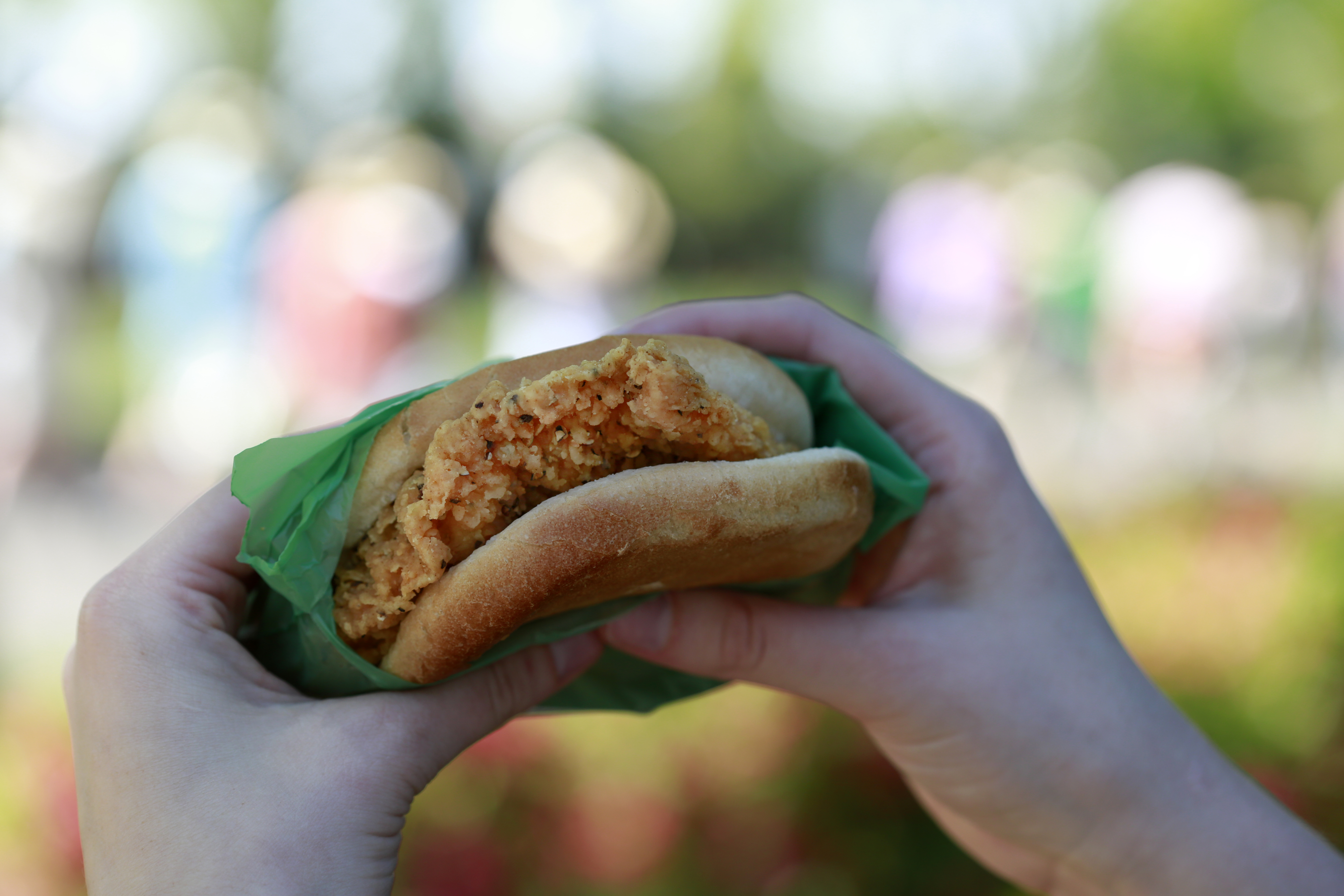 Hands holding a Masters chicken sandwich in a green wrapper