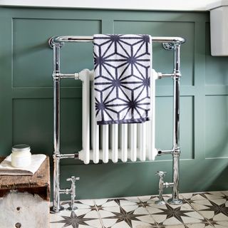 Heated towel rail and radiator against a green wood panelled wall with black and white patterned tile floor
