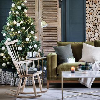Christmas tree with white baubles in front of worn wooden window shutters and behind wooden rocking chair