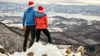 Couple wearing Santa hats standing on mountain