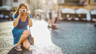 Lone tourist woman kneeling down with compact camera in Rome