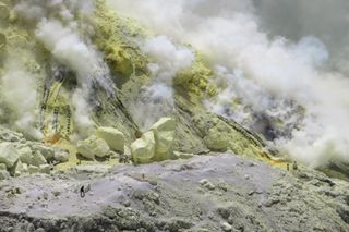Workers appear tiny next to enormous sulfur blocks on the dome at the southeast margin of Ijen Crater Lake.