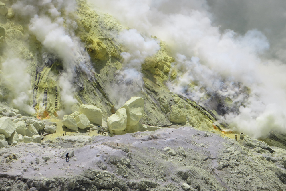 Workers appear tiny next to enormous sulfur blocks on the dome at the southeast margin of Ijen Crater Lake.