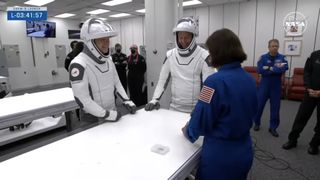 Two astronauts in white spacesuits play cards with an astronaut in a blue jumpsuit for Crew-9's launch.