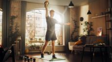 white man standing lifting kettlebell overhead living room setting