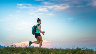 A woman wearing a rucksack walking along a ridge with grass, there is blue sky in the background