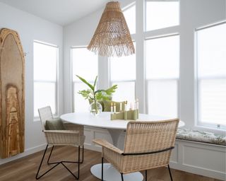 modern dining space with white walls, white circular table and two rattan chairs with woven pendant ceiling light