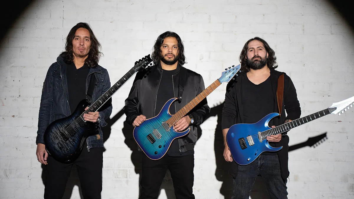 Periphery's Mark Holcomb, Misha Mansoor and Jake Bowen pose against a white wall with their signature guitars.