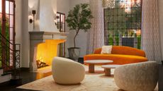 A design lounge features 1970s-inspired couches in warm hues of beige and orange, carpets, wide windows, and plants.