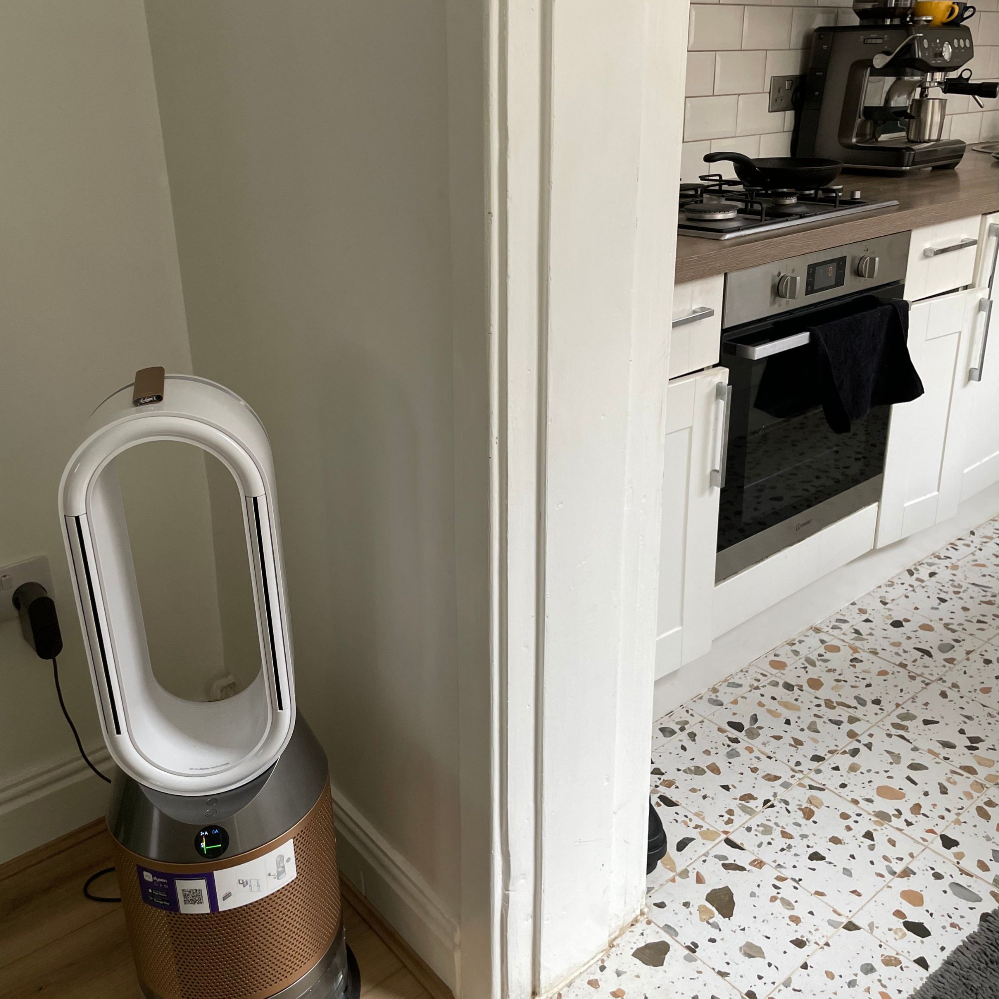 Dyson Purifier Humidify+Cool PH2 De-Nox standing in a living room, looking into a kitchen with a frying pan on the hob