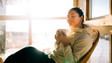 a woman relaxes in a chair, sipping coffee near windows