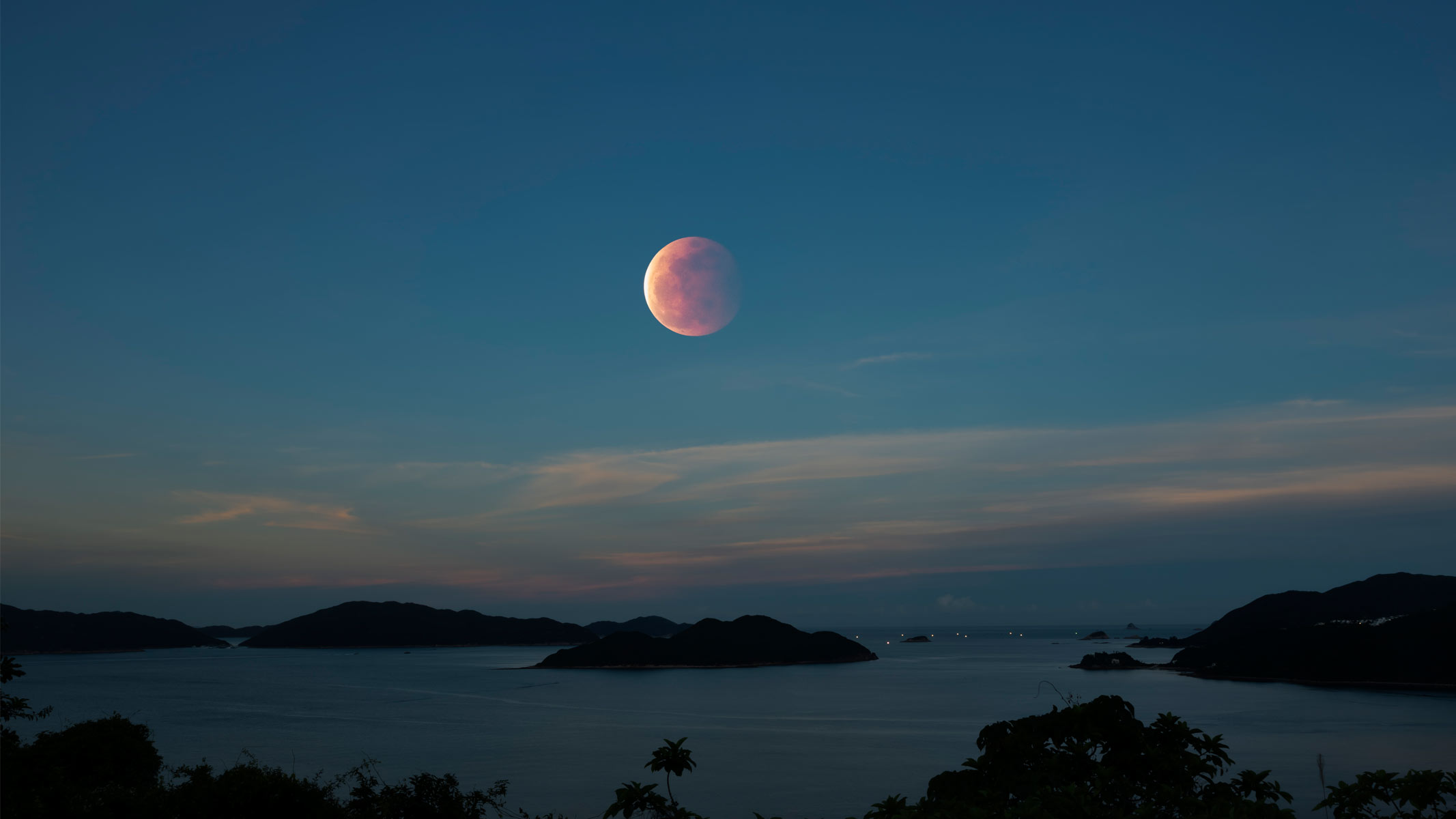 Lunar eclipse in a blue sky over a body of water.