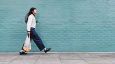 Young woman with mesh bag on footpath by turquoise brick wall 