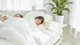 A couple sleeping peacefully in the WinkBed GravityLux mattress in a light bedroom