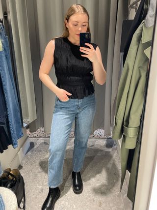 Woman in dressing room wears black top, blue jeans and black boots