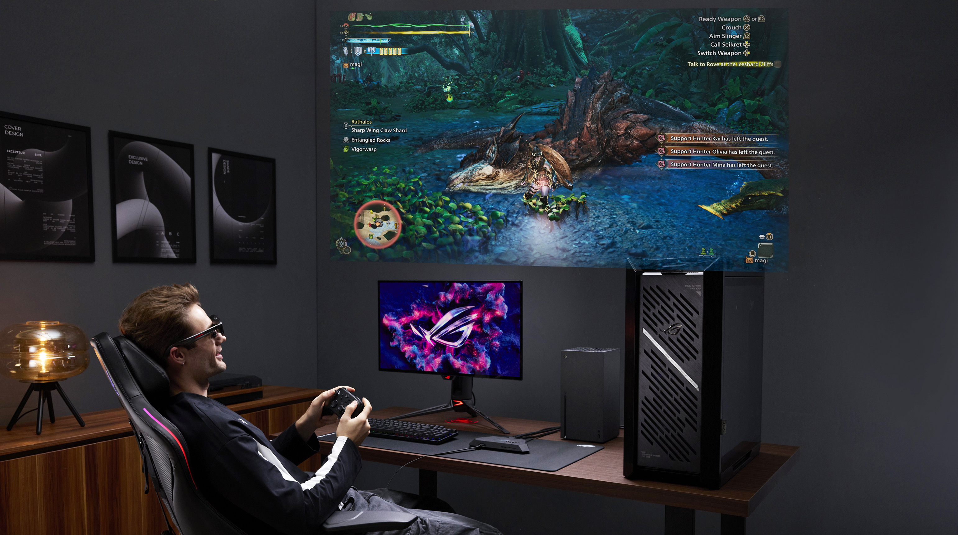 A man wearing sunglasses sits in a gaming chair, playing a game on a projector screen. The gaming setup includes a desktop PC and a monitor with a vivid logo.