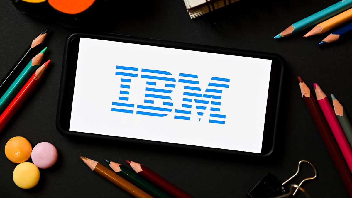 IBM logo appearing a smatphone which is set down on a desk surrounded by notebooks and different coloured pencils