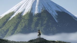 Atsu stands looking up over a huge mountain peak