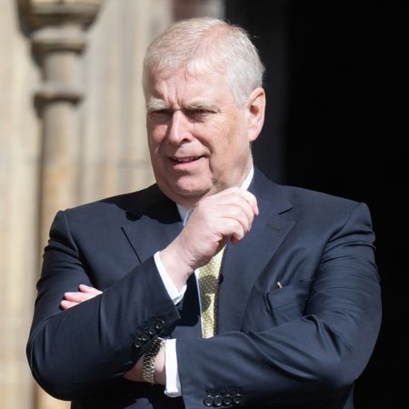 Prince Andrew looks bemused while looking at something wile wearing a suit with a white shirt and a golden tie, he has white gray hair